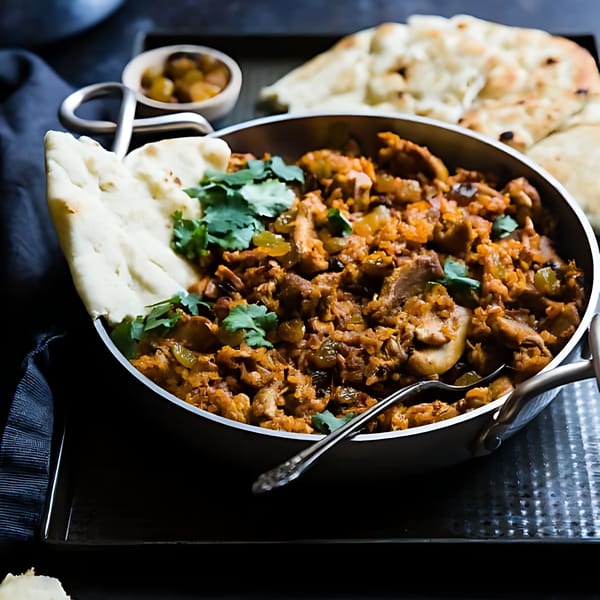 Spicy Chowk's Indian chicken curry in a metal pan with naan bread and cilantro.