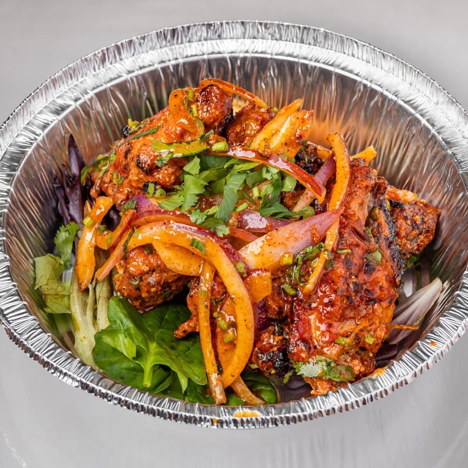 Spicy Chowk's Indian chicken dish with red onions and cilantro in a foil takeout container.