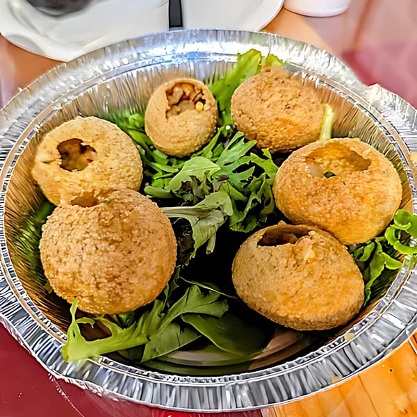 Six Indian pani puri, some filled, on a bed of greens in a foil container.