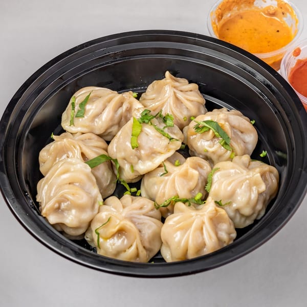 Steamed Indian momos garnished with fresh herbs, served in a black bowl with dipping sauces.