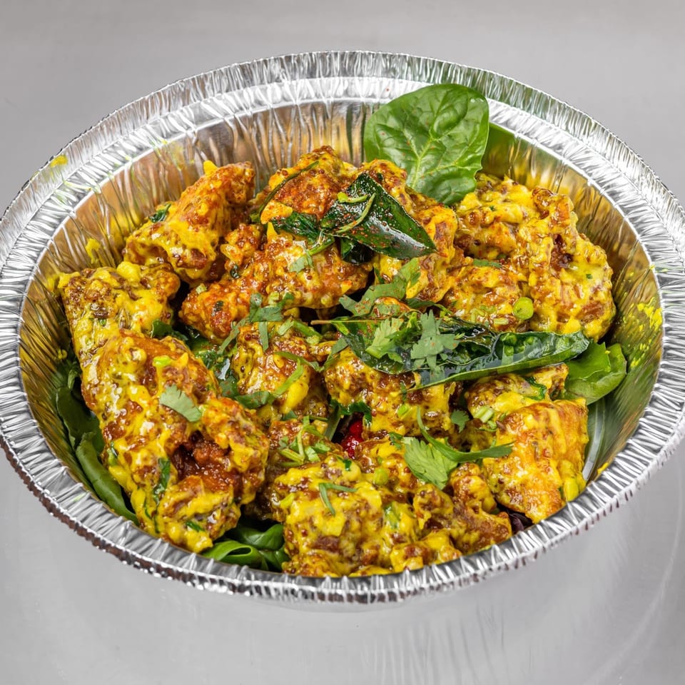 Spicy Chowk's Indian chicken dish, coated in a rich yellow sauce, garnished with fresh herbs in a foil container.
